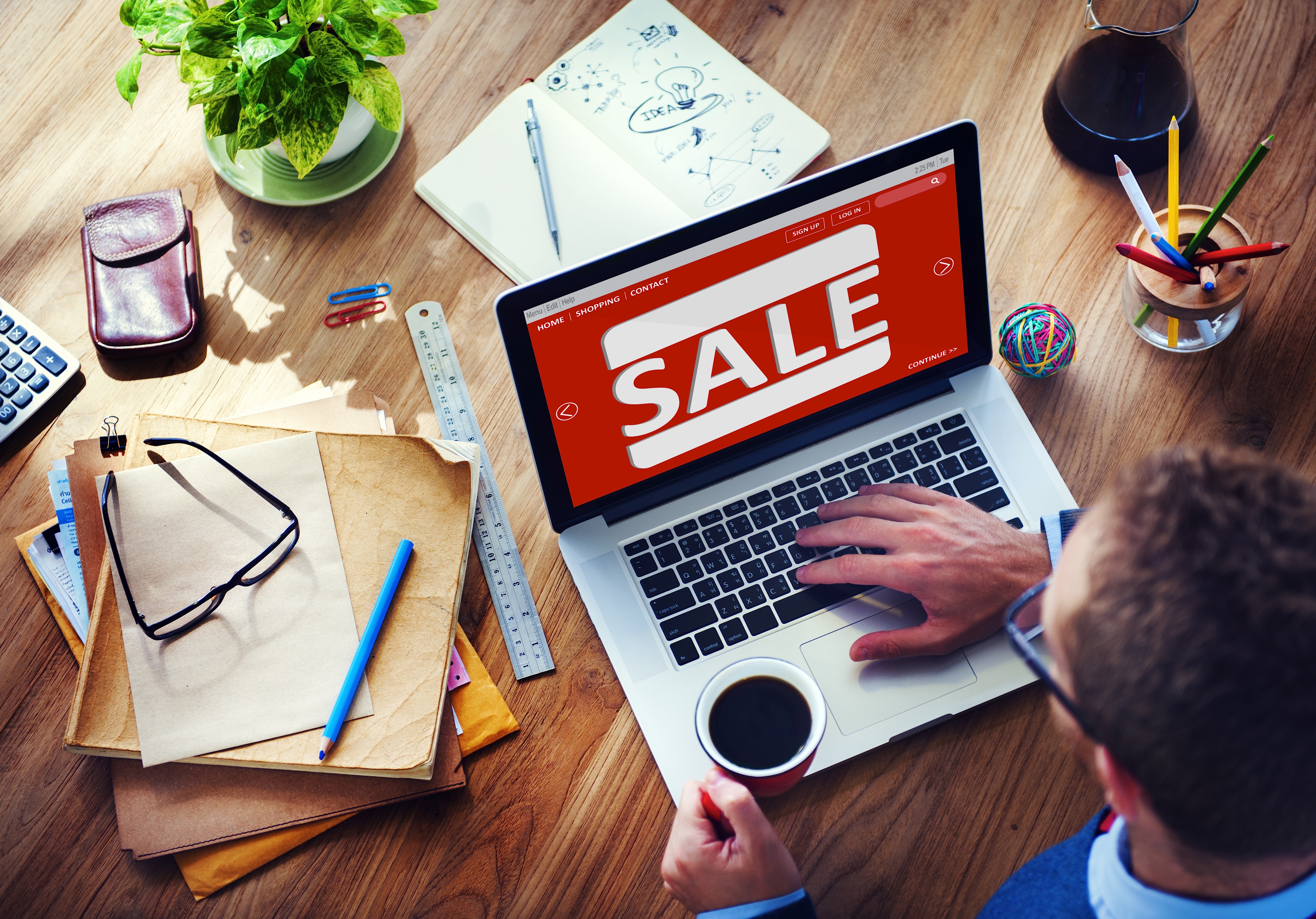 Man working on computer with sale sign on it and coffee in hand.