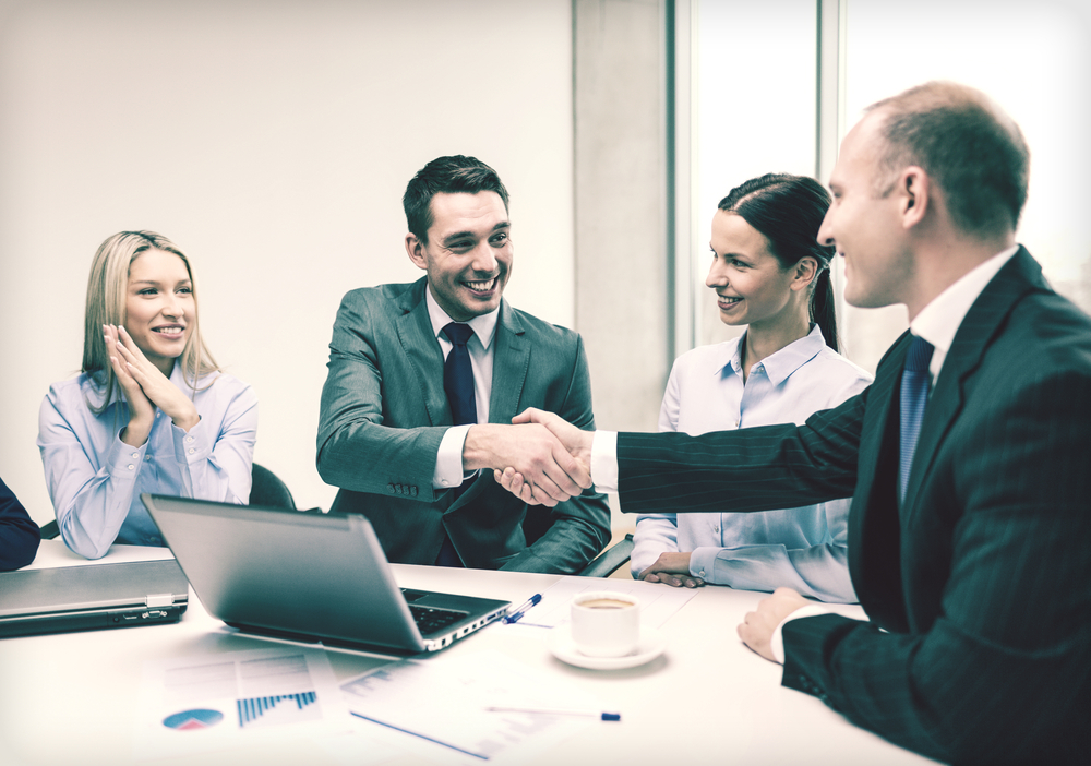 Men shaking hands at table.